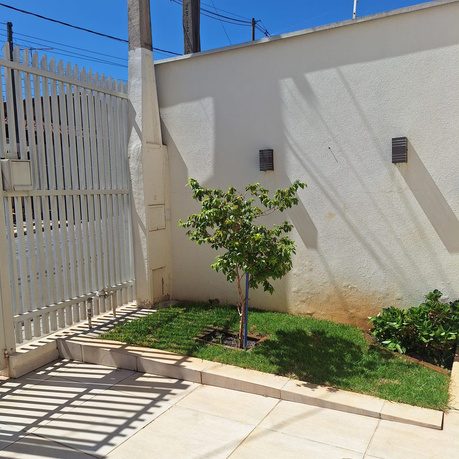 Jardim externo com árvore e portão de segurança