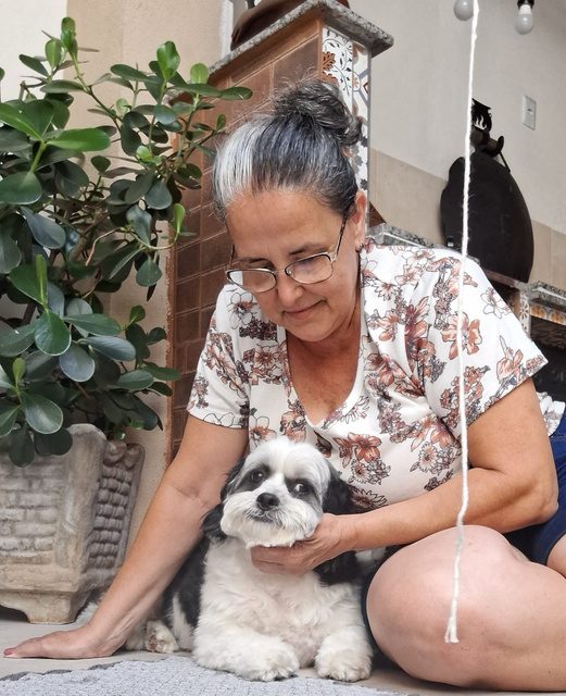 Cuidadora carinhosa abraçando um shih-tzu preto e branco no jardim