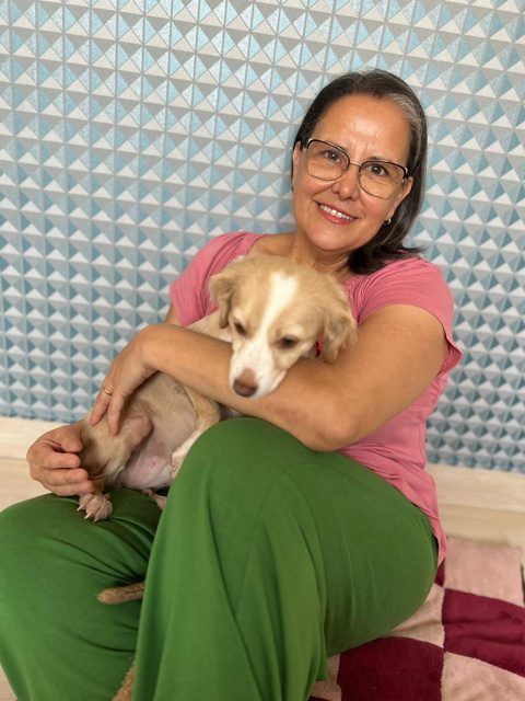 Vera sentada abraçando um cachorro filhote bege