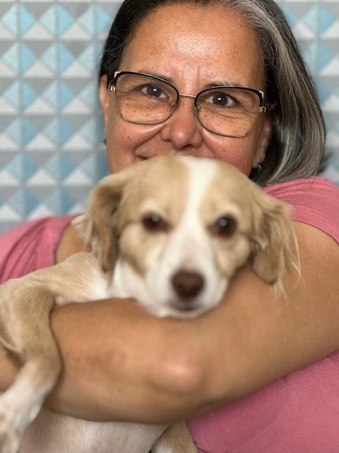 Vera sorrindo enquanto abraça um cachorro de pelo claro